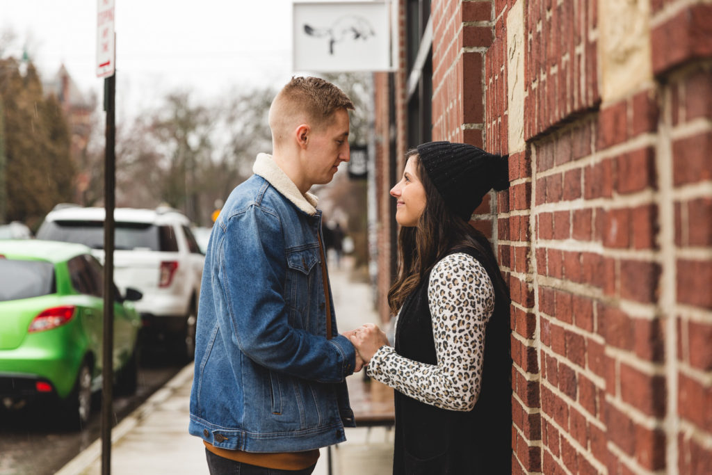 Couple holding hands against a brick wall on an old village street for engagement photos