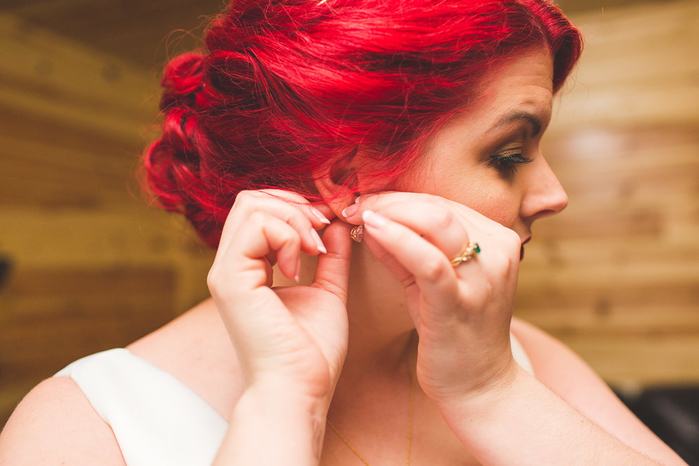 bride with red hair putting in her earrings in log cabin on wedding day in hocking hills