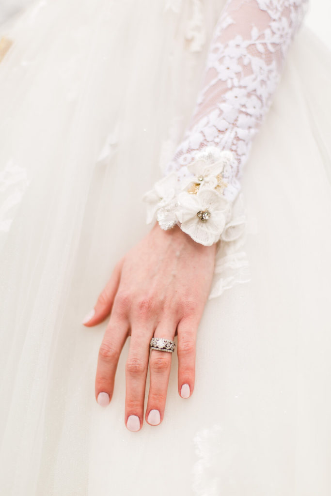 bride hand with engagement ring in flowery white wedding dress 