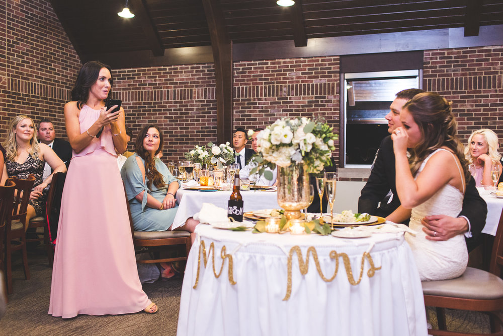 maid of honor giving toast speech at wedding reception while bride and groom cry with tears in their eyes