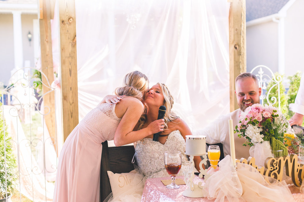 maid of honor hugs bride after giving toast speech at wedding reception bride crying