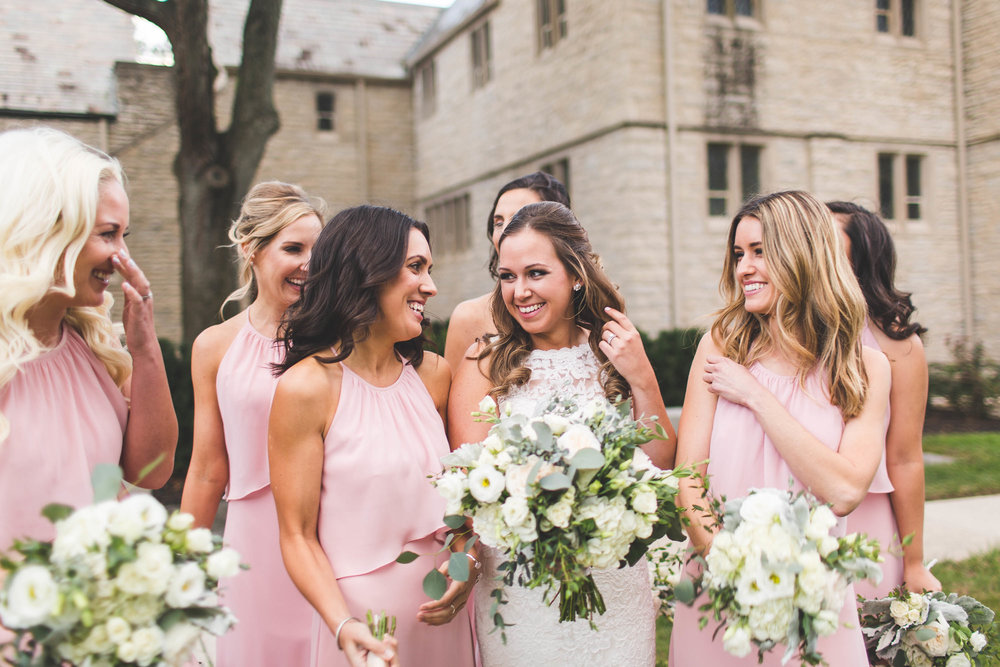 bride and bridesmaids laughing with flowers outside church