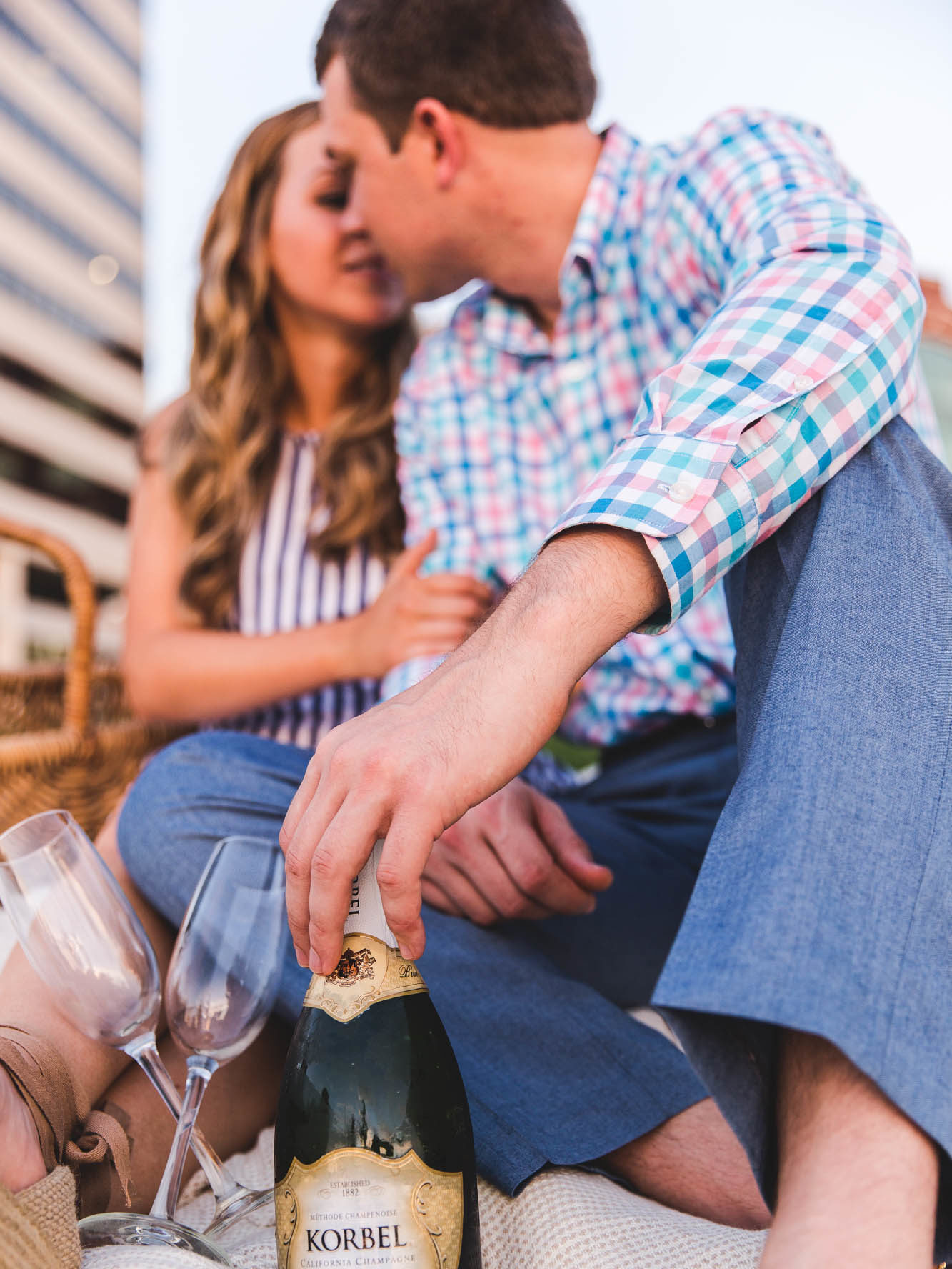 Couple toasting champagne kissing on a picnic blanket in front of a city skyline
