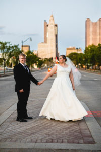 bride and groom hold hands and pull each other as they stand in busy urban street in downtown columbus ohio