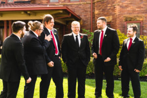 groom and groomsmen laugh at each other in black suits while taking photos in columbus ohio