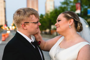 Bride brushes hand on groom's face in busy urban street at sunset in Columbus, Ohio