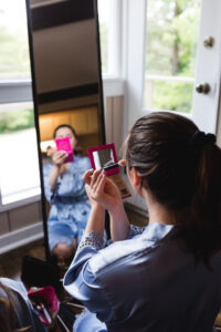 a bridesmaid applying eye shadow in front of a rectangle mirror and windows