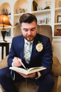 Groom sitting in an armchair with a rose reading a journal