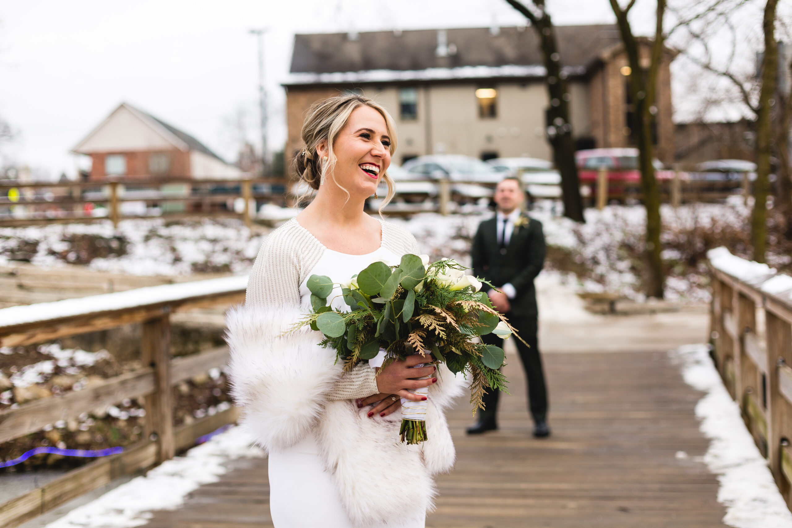 Bride turns around for first look on her wedding day on a snowy day in a park on a bridge