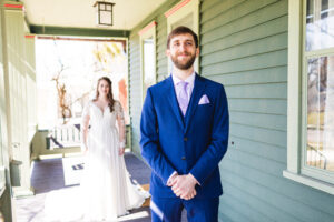 Groom waiting for his first look with a bride on a green porch in the background