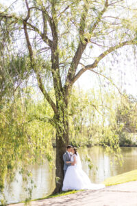 bride and groom kissing under a weeping willow tree in front of a pond