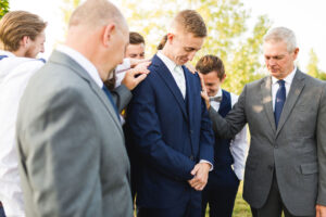Family and friends praying for the groom before his wedding day outside