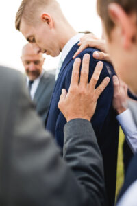 hand on the shoulder of a groom on his wedding day outside