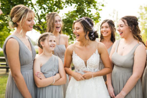 bridesmaids laugh with the bride during portraits outside in front of a tree