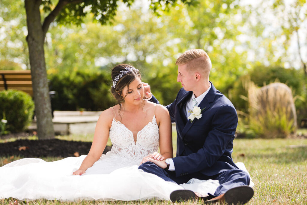 groom caresses bride while sitting in grass on a summer day