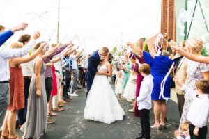 Outside a bride and groom have a send off with guests holding ribbon wands