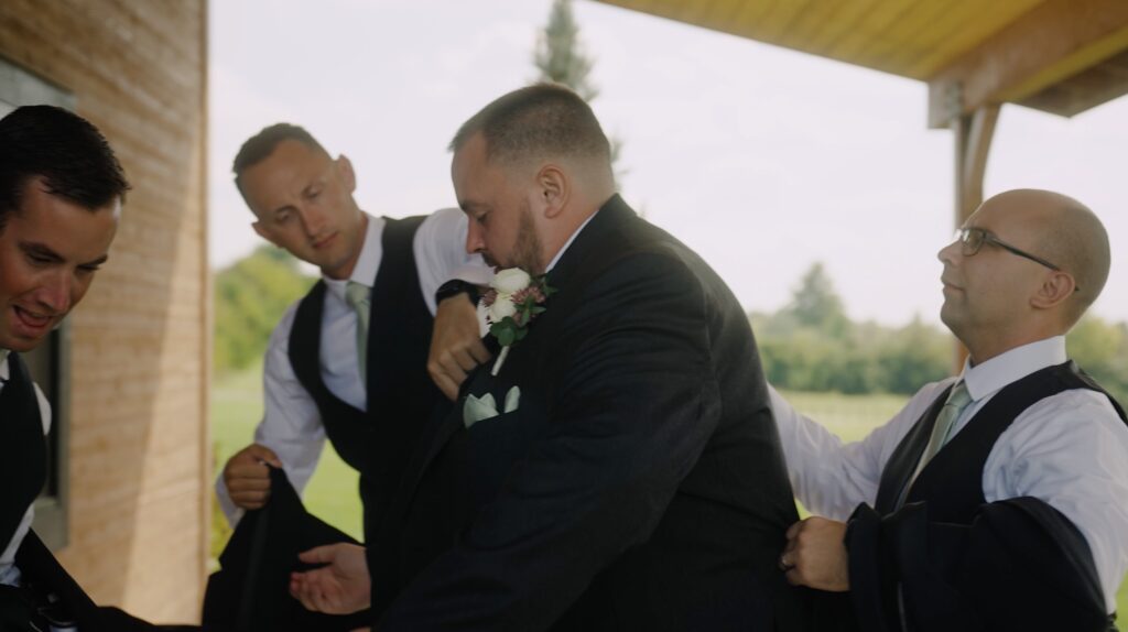 Guys getting groom prepped for his wedding outside of a wooden log cabin at Stone Valley Meadows