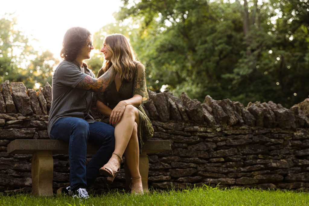 a man pulls a woman in for a kiss with a stone fence behind them