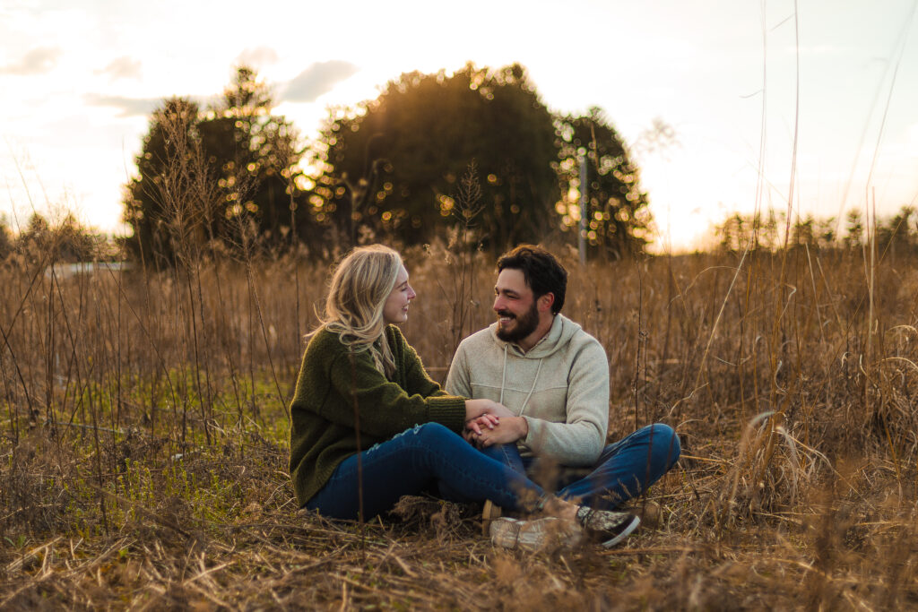a woman and man sit together in a field during an engagement session in ohio